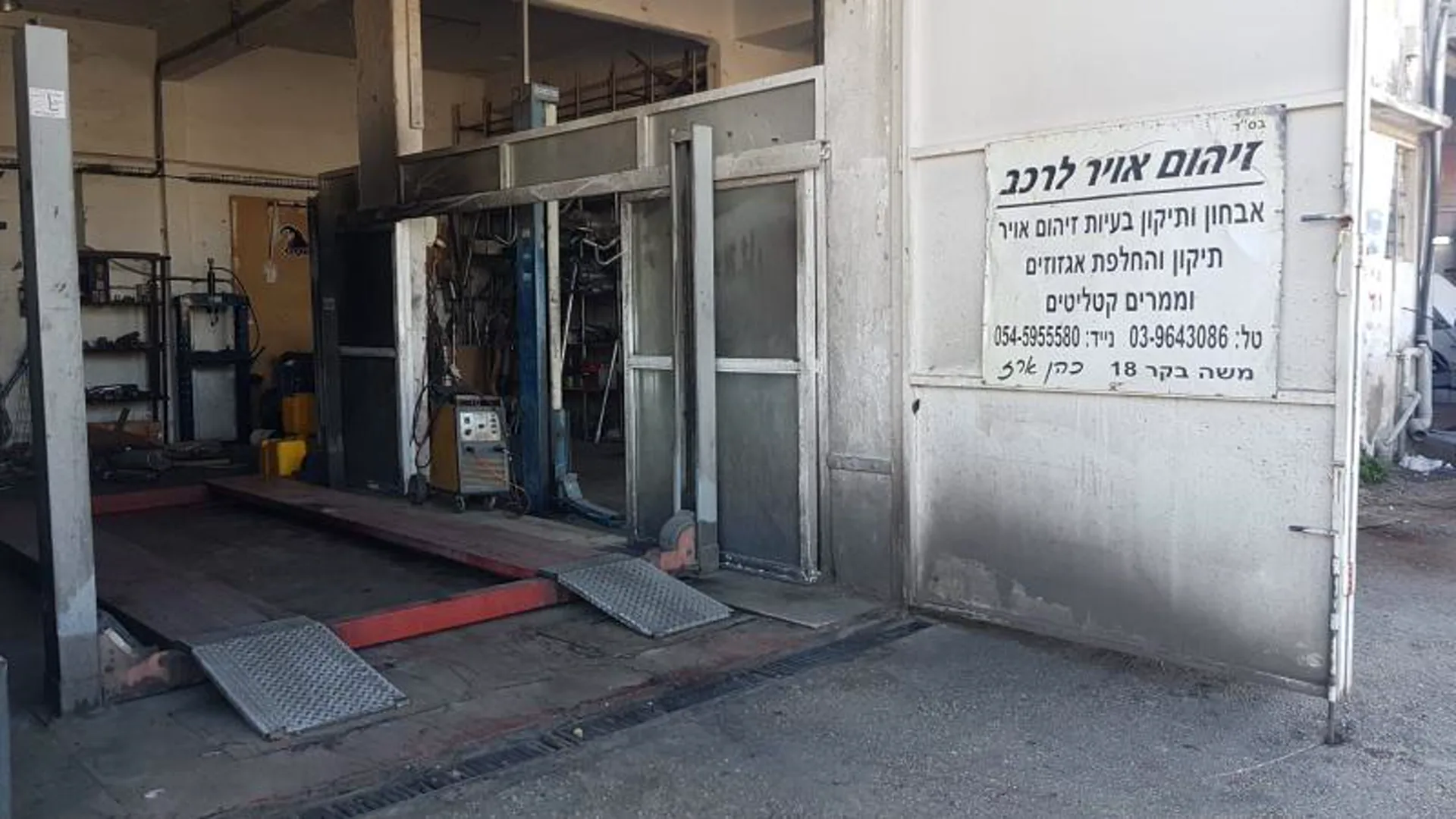 כניסת המוסך עם רמפות הרמה ושלט השירותים — אבחון ותיקון בעיות זיהום אוויר, אגזוזים וממירים קטליטיים